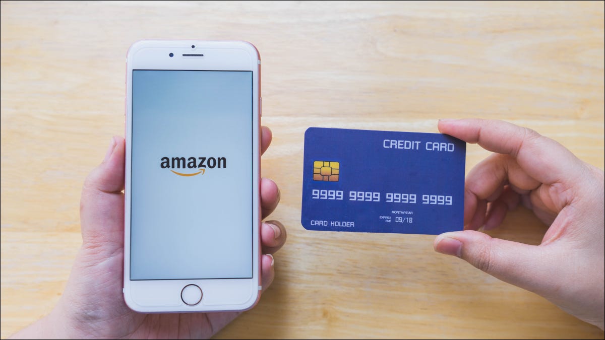 As mãos de uma pessoa segurando um cartão de crédito e um smartphone mostrando o logotipo da Amazon.