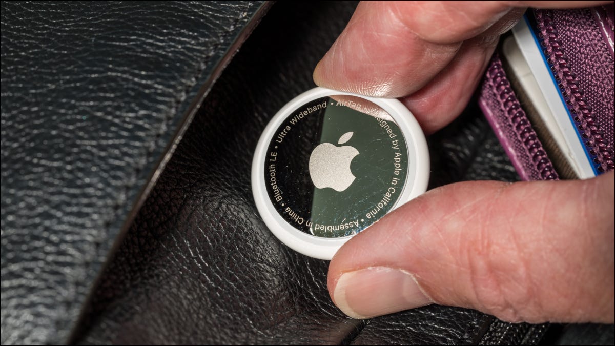 Close de uma Apple AirTag sendo colocada na bolsa de couro de alguém.