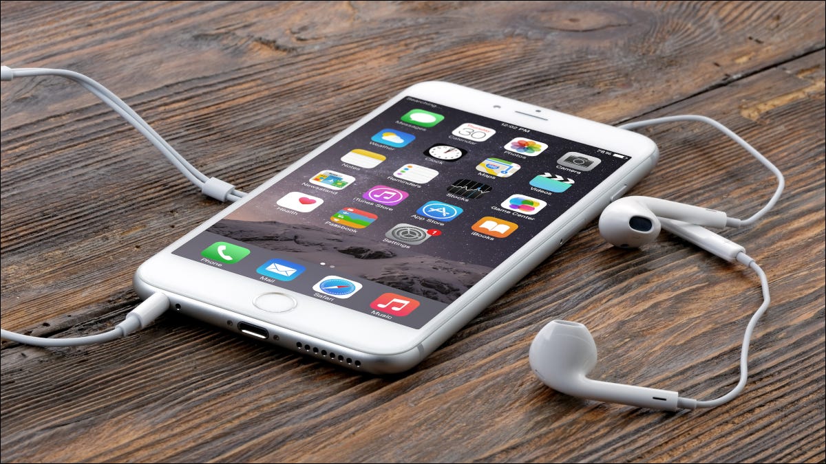 Um iPhone 6 Plus com fones de ouvido conectados em uma superfície de madeira