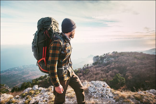 Um homem subindo uma montanha, com uma paisagem acidentada ao fundo.