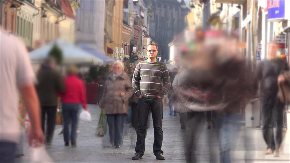 Homem de pé em uma calçada de rua movimentada enquanto as pessoas passam rapidamente.