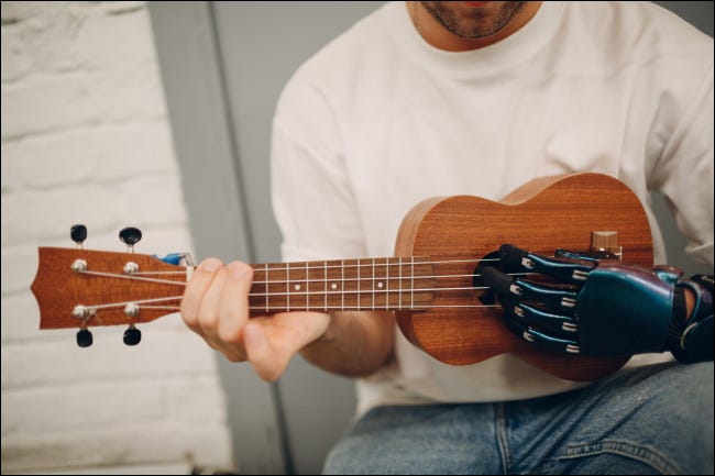 Um homem tocando um ukelele com uma mão protética.