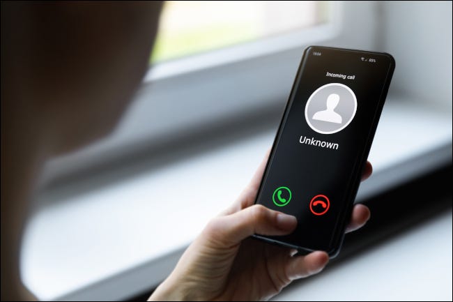 Mulher segurando um smartphone que mostra uma chamada recebida de um número desconhecido.