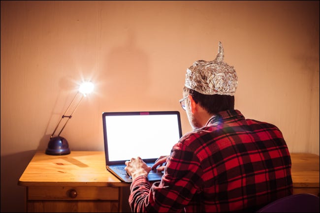 Jovem sentado em uma mesa com um laptop e um chapéu de folha de estanho.