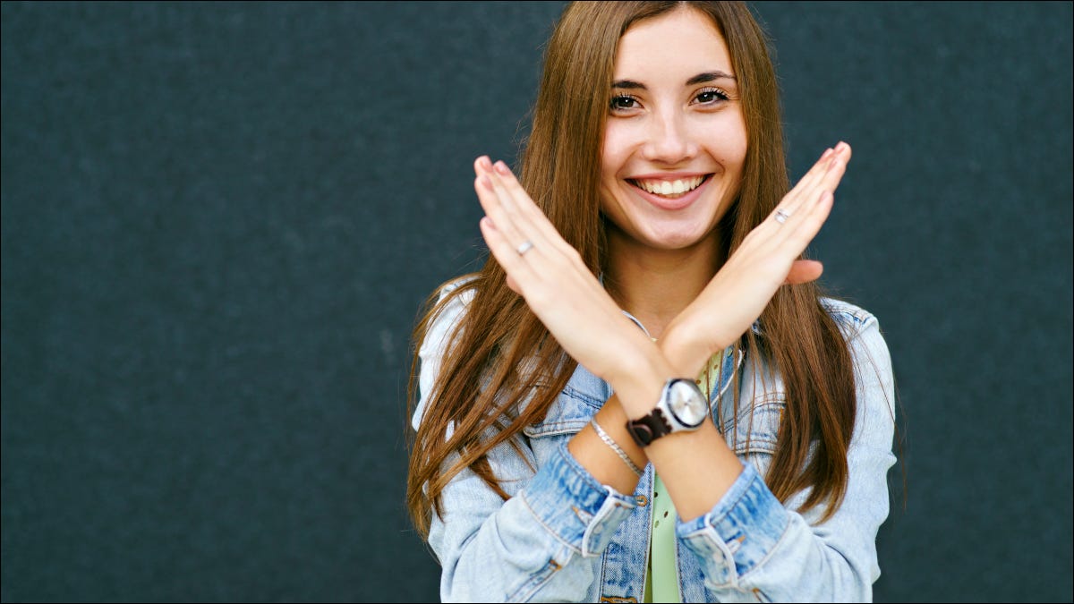 Jovem sorrindo e cruzando os braços para formar um "X".