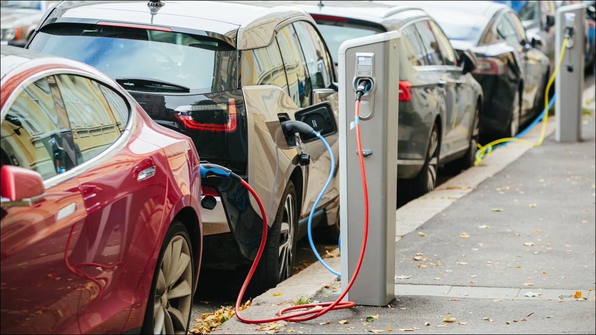 Carros elétricos estacionados em uma rua, ligados a estações de recarga.