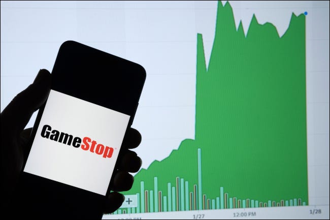 Um smartphone mostrando o logotipo da GameStop na frente de um gráfico de aumento do valor das ações.