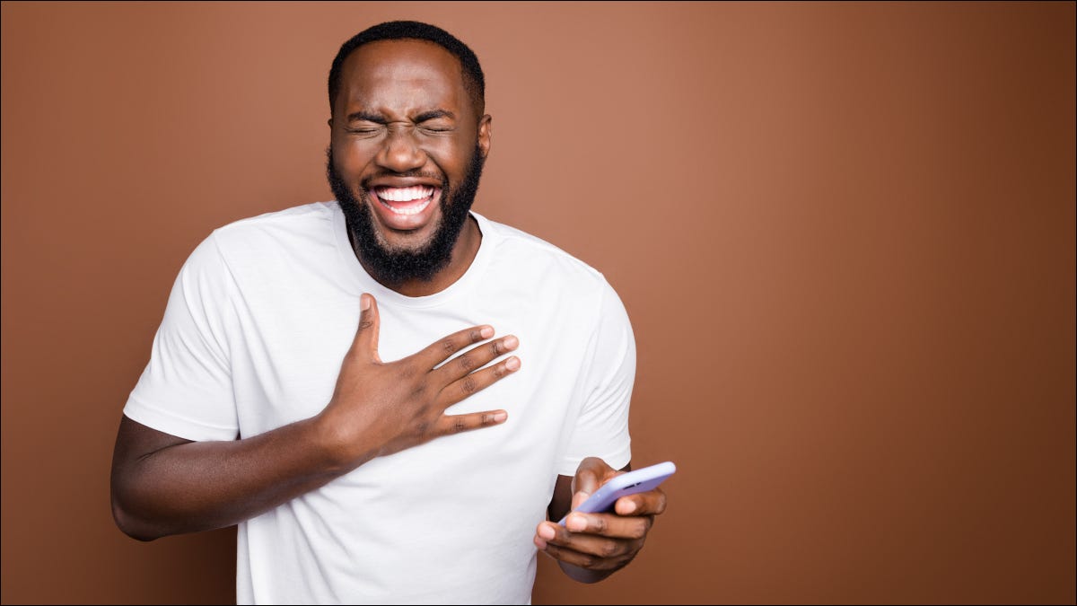 Homem rindo enquanto segura um smartphone.