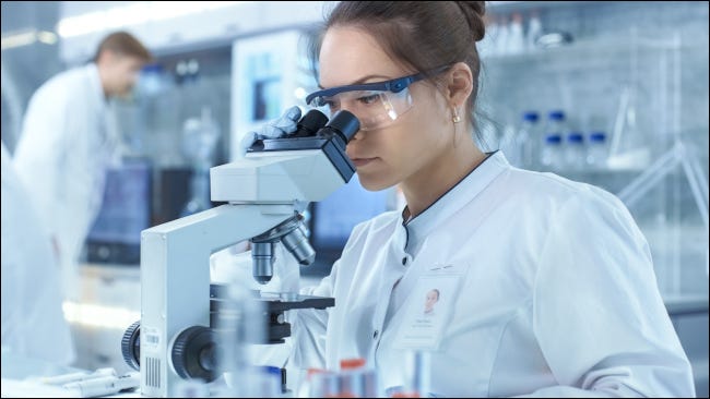 Um cientista em um laboratório olha através de um microscópio.