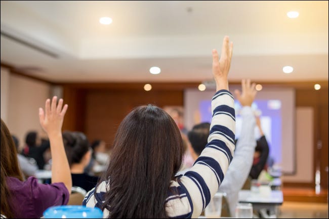 Empresários levantando as mãos para fazer perguntas em uma conferência.