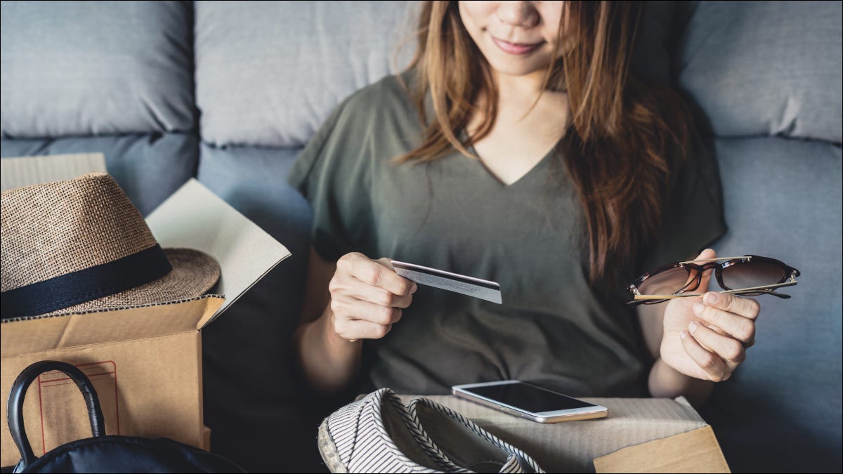 Mulher abrindo mercadorias compradas on-line e olhando o cartão de crédito.