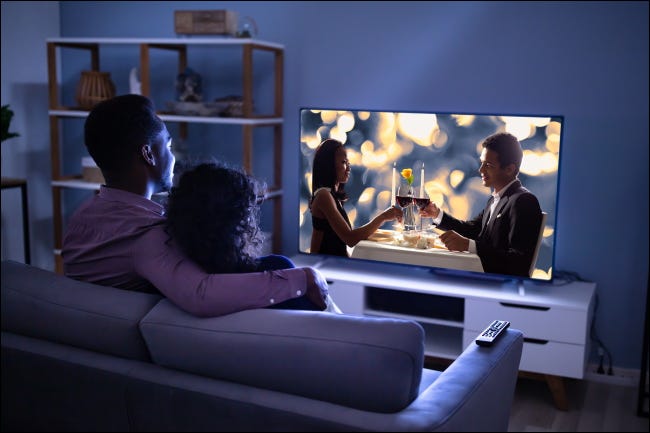 Um casal assistindo TV em um sofá.