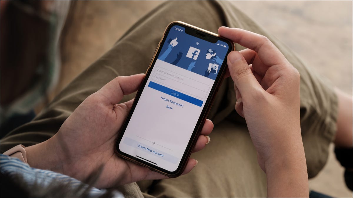 Pessoa segurando um iPhone com a tela de login do aplicativo do Facebook visível.