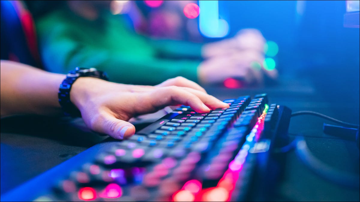 Close da mão de uma pessoa em um teclado com iluminação RGB.