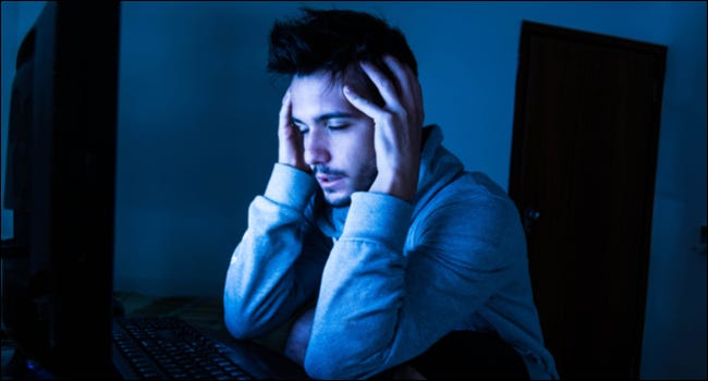 Homem parecendo estressado ou exausto ao usar um computador no escuro.
