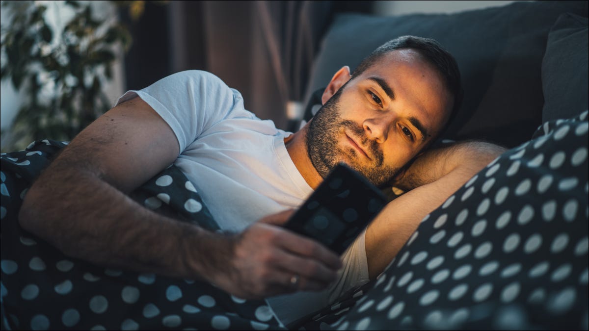 Homem usando um smartphone enquanto estava deitado na cama.