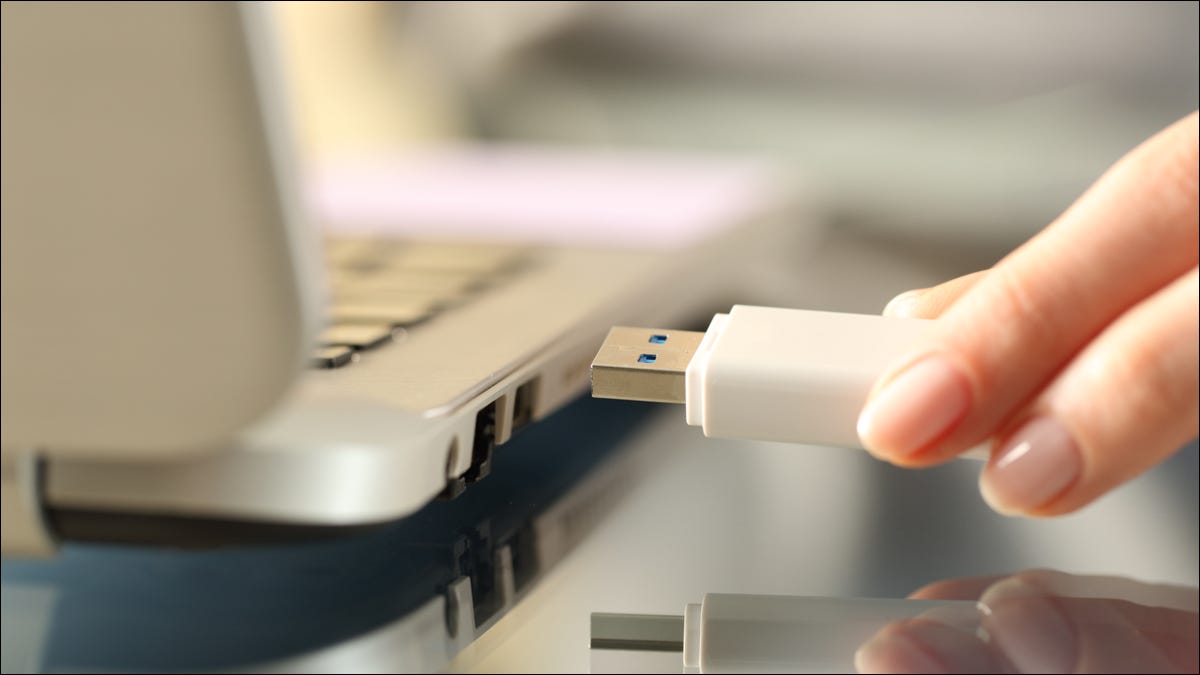 Closeup da mão de uma mulher conectando uma unidade USB em um laptop.