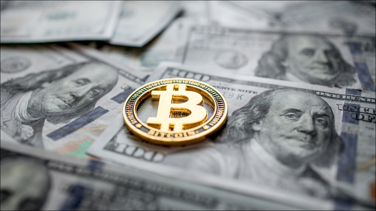 Uma moeda representando Bitcoin em cima de dólares americanos.