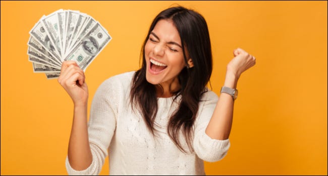 Uma mulher com uma expressão animada segurando um leque de notas de cem dólares.