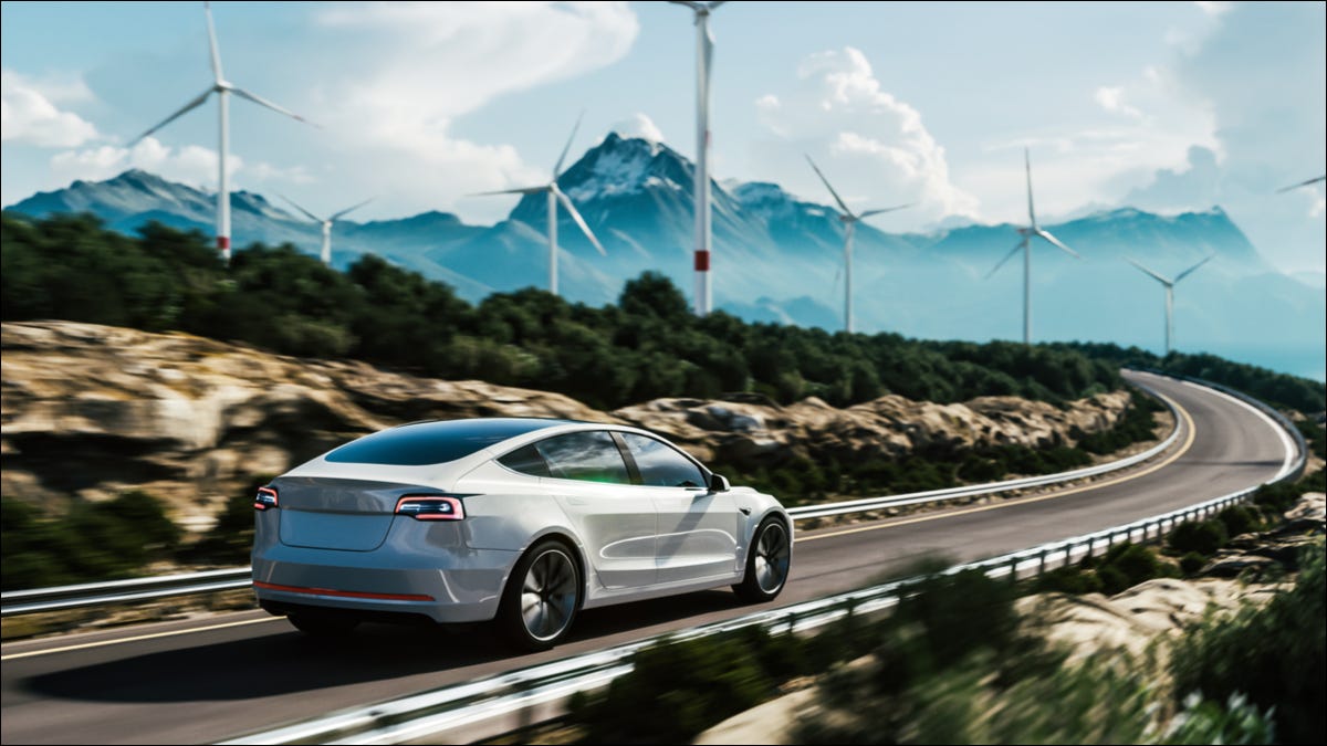 Um carro elétrico dirigindo por uma estrada com turbinas eólicas ao fundo.