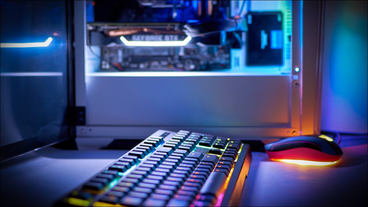 Teclado iluminado por RGB com uma torre de PC iluminada em segundo plano.