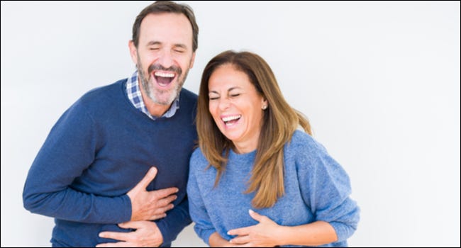 Um casal segurando suas barrigas em risadas.