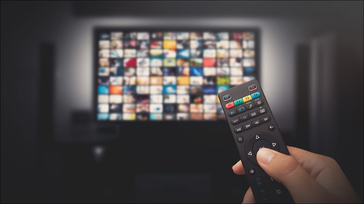 Close de um controle remoto de TV na mão de uma pessoa, com uma tela de TV mostrando opções de multimídia em segundo plano.