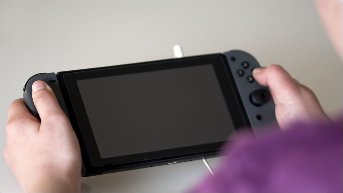 Pessoa pressionando botões em um Nintendo Switch com a tela desligada.