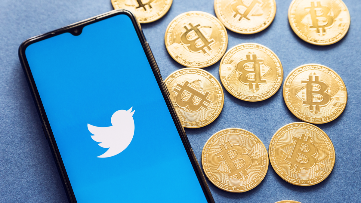 O aplicativo do Twitter em um smartphone com moedas Bitcoin ao lado.