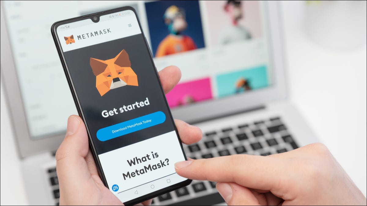 MetaMask em um telefone com um laptop e um navegador da Web em segundo plano.