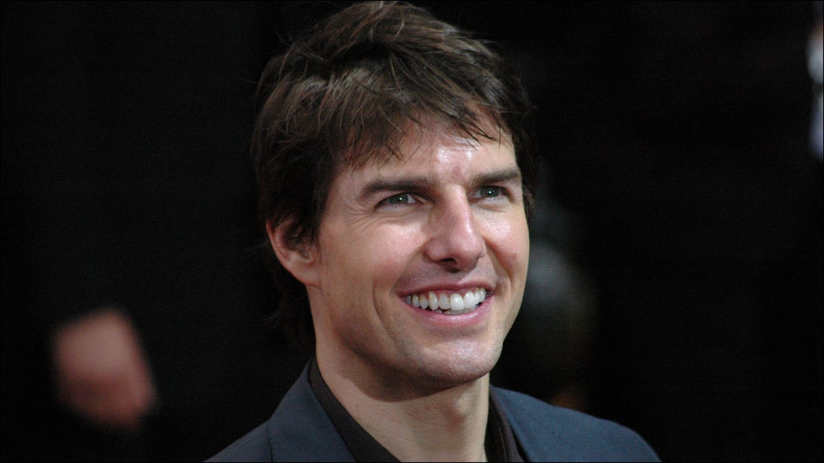 O ator Tom Cruise sorrindo para as câmeras na estreia de um filme.