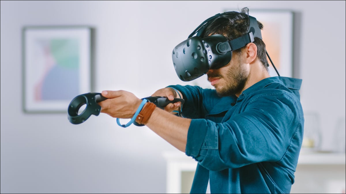 Um homem usando um fone de ouvido VR e mirando com controladores.