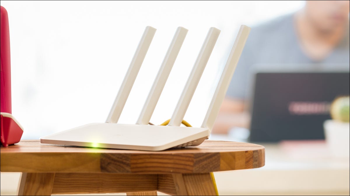 Roteador Wi-Fi branco em uma mesa com um homem usando um laptop em segundo plano.