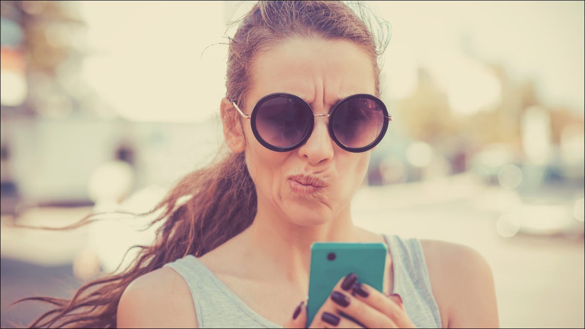 Mulher olhando para seu smartphone com uma expressão descontente ou cética.