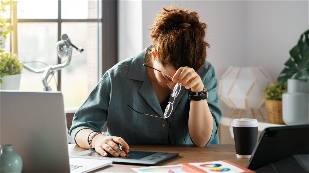 Mulher em um escritório com dor de cabeça ao usar tecnologia.
