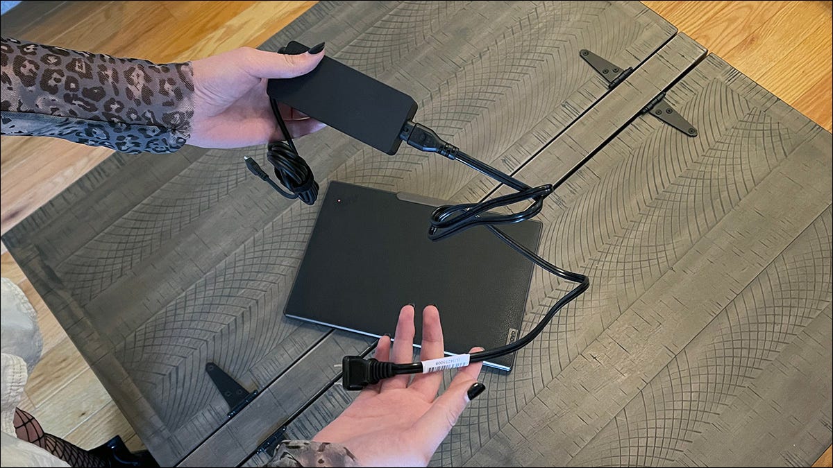 Garota acima de um notebook com tela sensível ao toque Lenovo ThinkPad Z13 Gen 1 fechado segurando seu adaptador CA