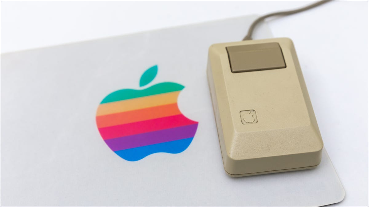 Um rato de computador de Apple do vintage em um mousepad com o logotipo de Apple do arco-íris.