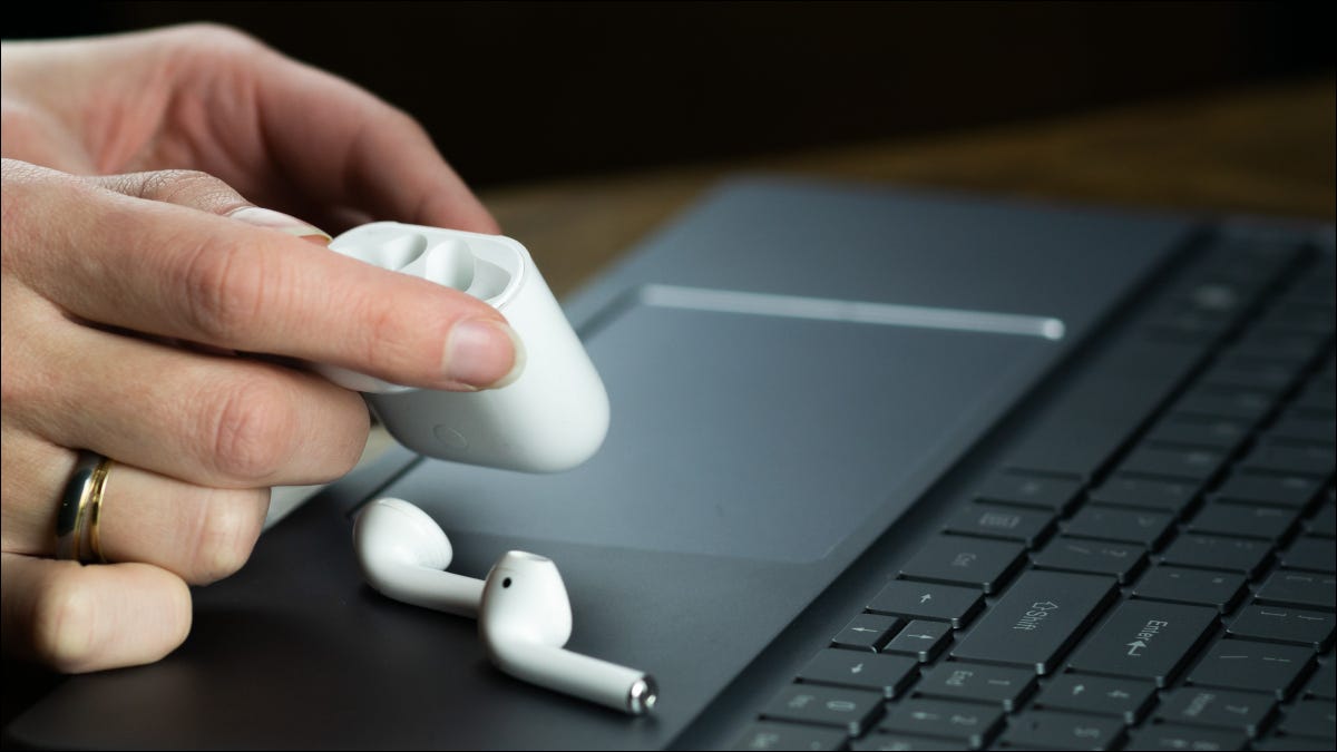 Mãos de uma pessoa segurando um estojo Apple AirPods com os fones de ouvido em cima de um laptop preto.