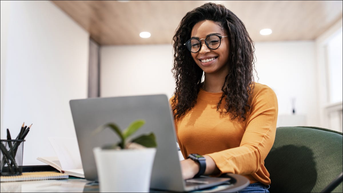 Jovem mulher de óculos e sorrindo enquanto digita em um laptop.