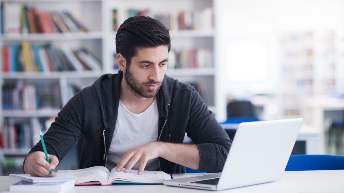 Jovem estudando em uma biblioteca e usando um laptop.