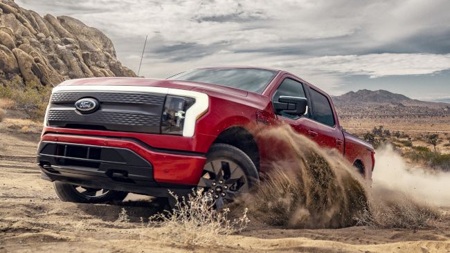 Uma caminhonete elétrica Ford F-150 Lightning vermelha 2022 dirigindo por um deserto.