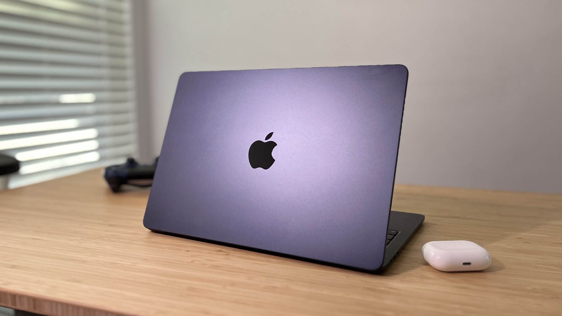 Apple MacBook Air M2 apoiado na mesa ao lado do AirPods Pro e do controlador PS4.