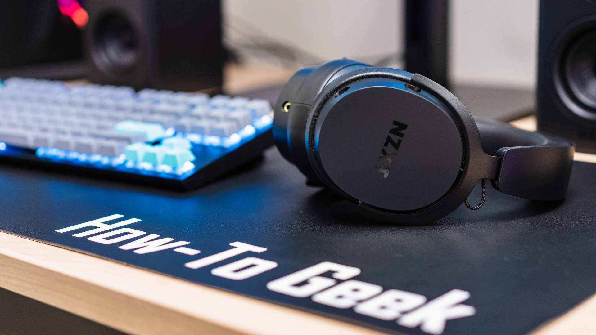 O NZXT Relay Headset colocado próximo a um teclado em um tapete de mesa How To Geek