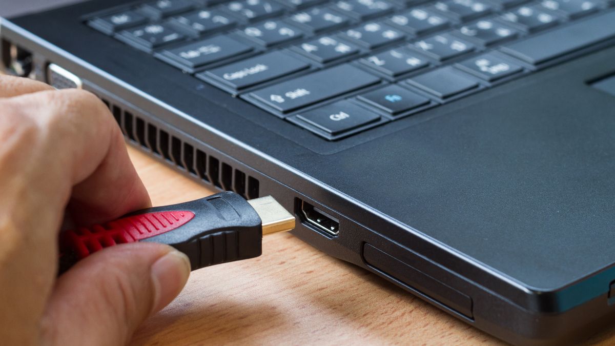 Pessoa conectando um cabo na lateral de um laptop