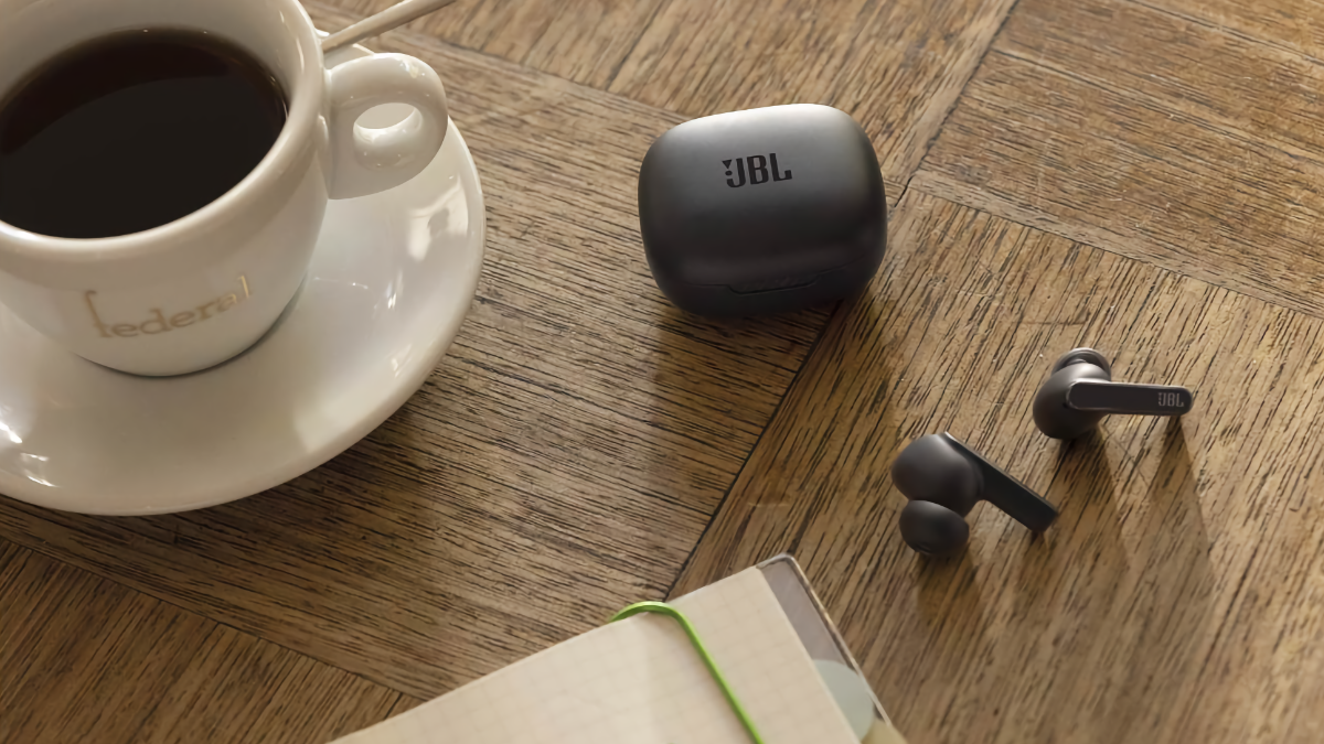 Fones de ouvido JBL Live Pro 2 sobre uma mesa ao lado de uma xícara de café e um notebook