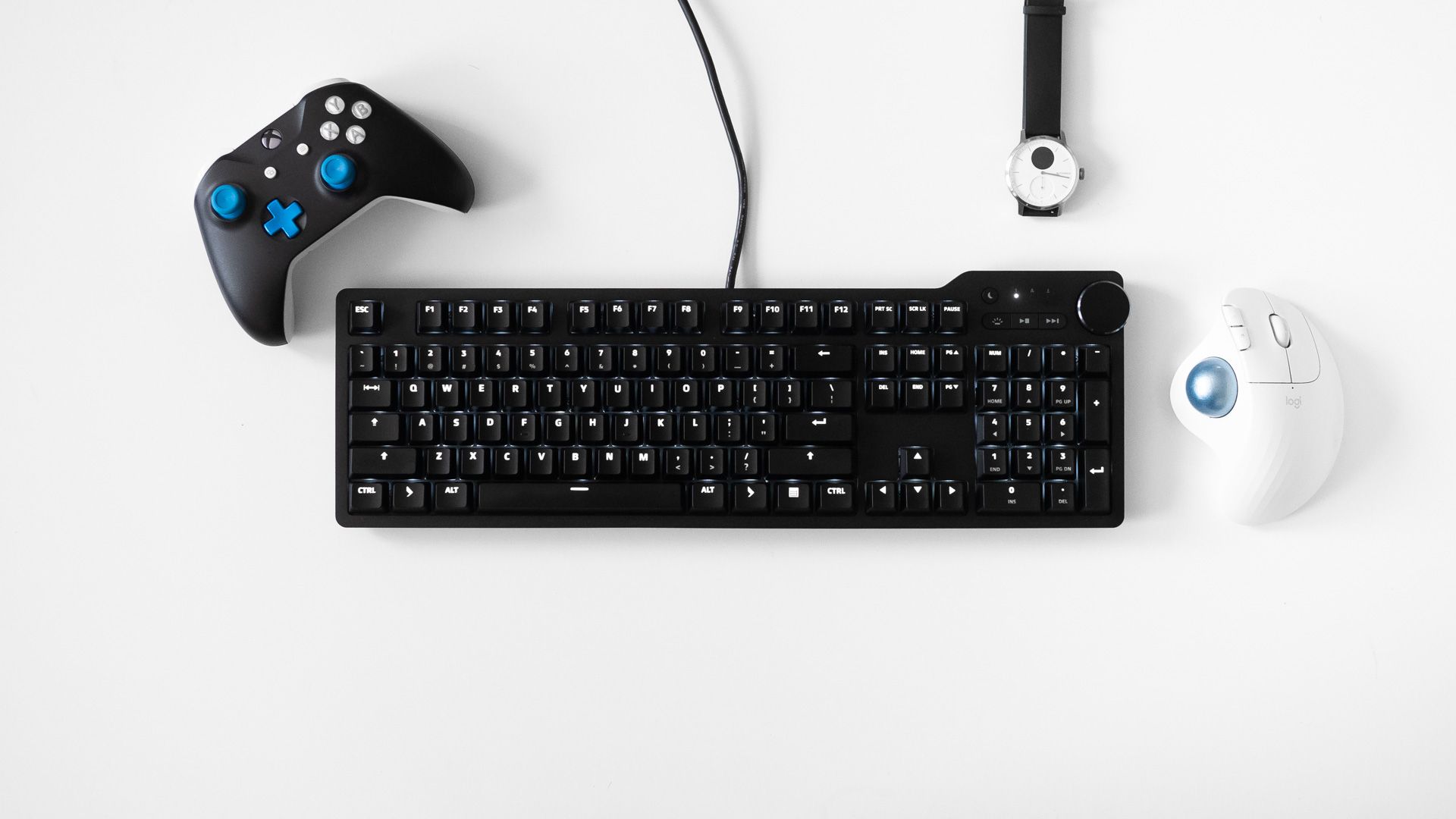 Das Keyboard 6 Professional com um controlador de xbox, relógio e mouse trackball ao seu redor
