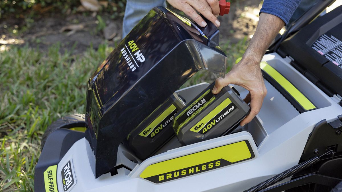 Uma pessoa colocando uma bateria em seu cortador de grama Ryobi.