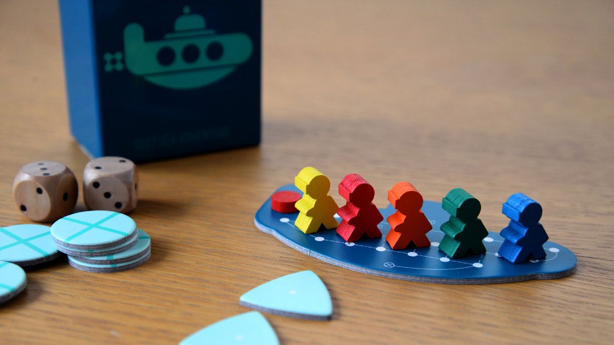 Um submarino de papelão contendo pequenos modelos de jogadores de madeira do jogo Deep Sea Adventure.