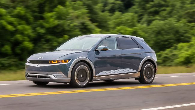 O carro elétrico Hyundai IONIQ 5 2022 dirigindo por uma estrada em frente às árvores.