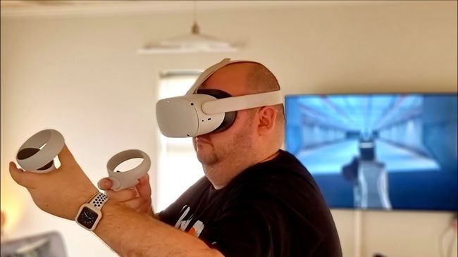 Um homem usando um headset Quest VR com imagens transmitidas para uma TV na parede.